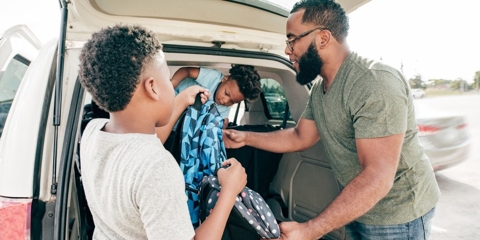 man and two kids getting backpacks out of the car